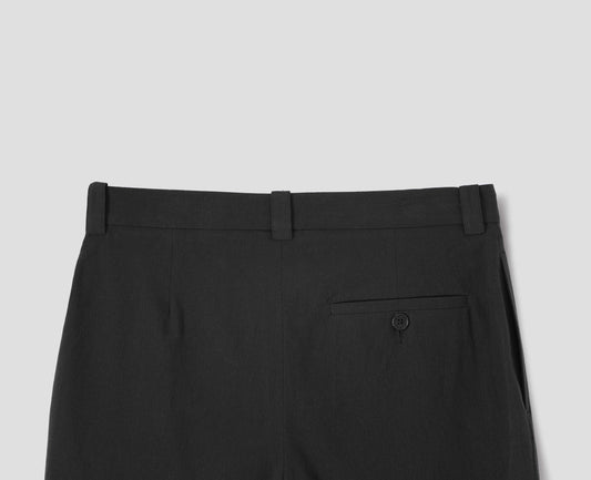 Black cotton trousers with side pockets and horn button-fastening welt back pocket. Back flat lay view.