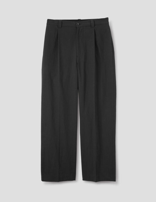 Black cotton trousers with horn button and zip fly fastening, regular belt loops, single pleats, hidden ticket pocket and side pockets. Front flat lay view.