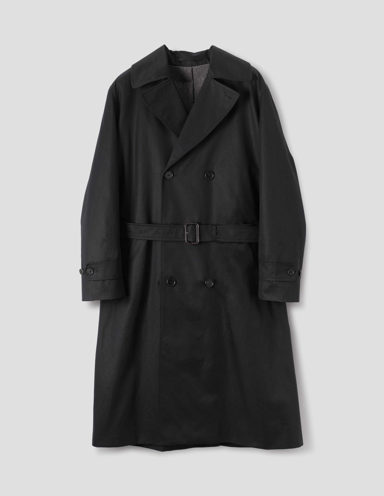 Black double breasted cotton coat with horn buttons, revere collar, internal hanger loop, detachable belt, button tab detailing on sleeves and wide single welt front pockets. Front flat lay view.