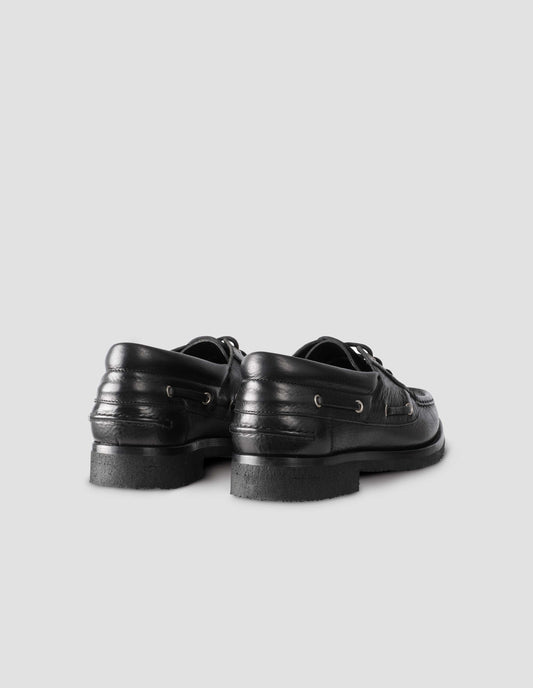 A pair of black leather deck shoe with padded heel collar and crepe sole. Back flat lay view.