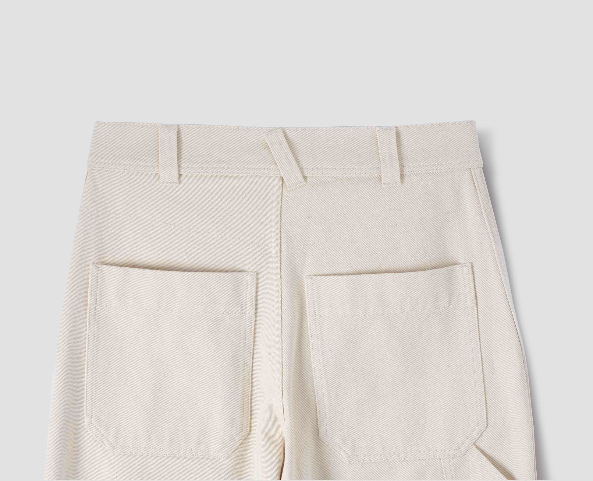 Off white trousers with belt loops and large patch back pockets. Back flat lay view.