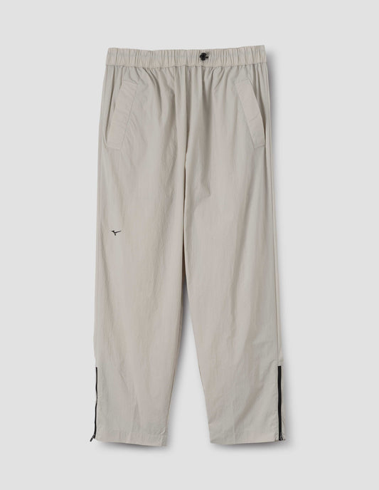 Light grey lightweight trousers with elasticated waist with toggle cinch adjuster, zipper on lower leg and slant pockets. Front flat lay view.