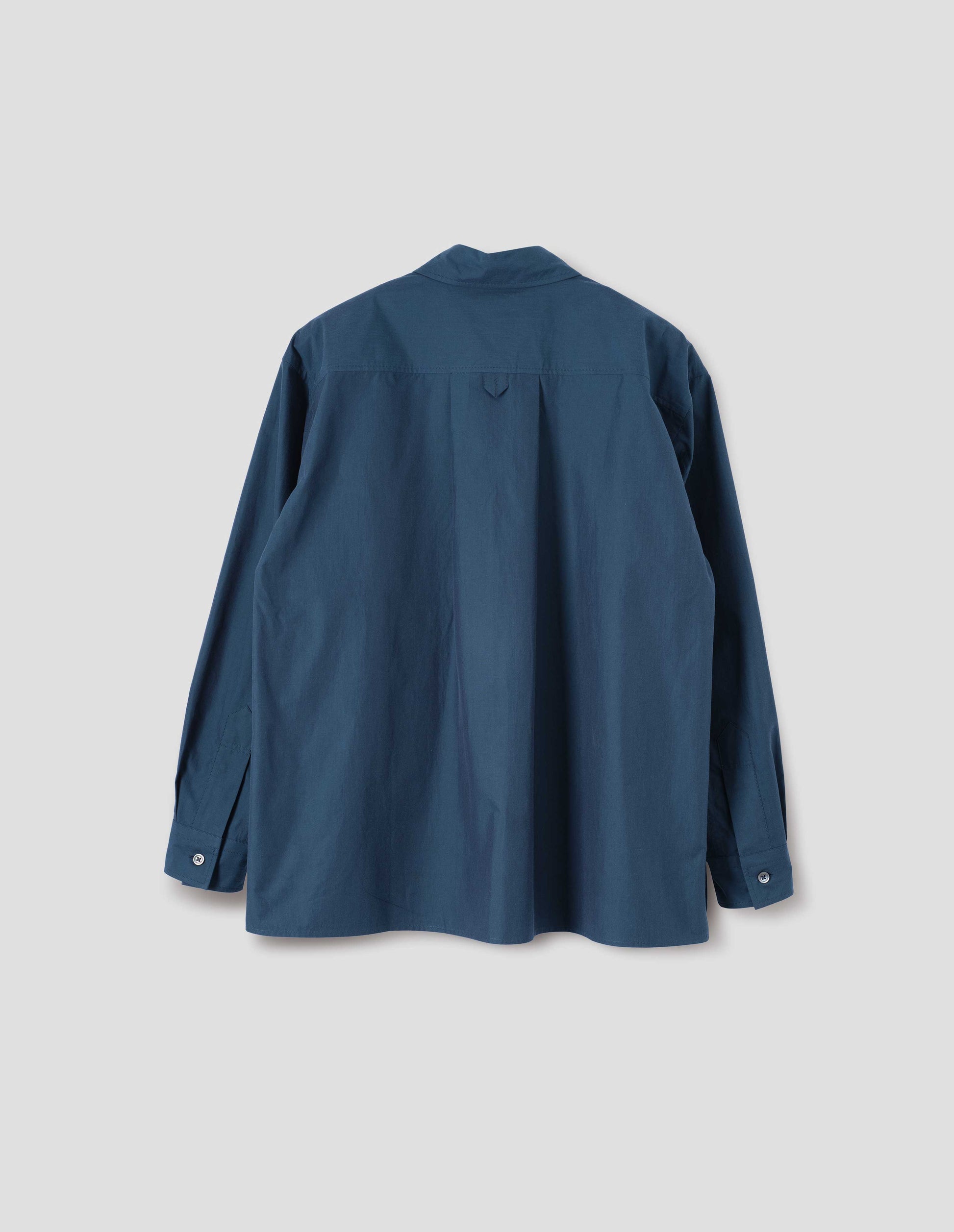 Blue shirt with deep side split vents, elongated back, box pleat and hanger loop detail on back yoke, mother of pearl buttons on cuffs. Back flat lay view.