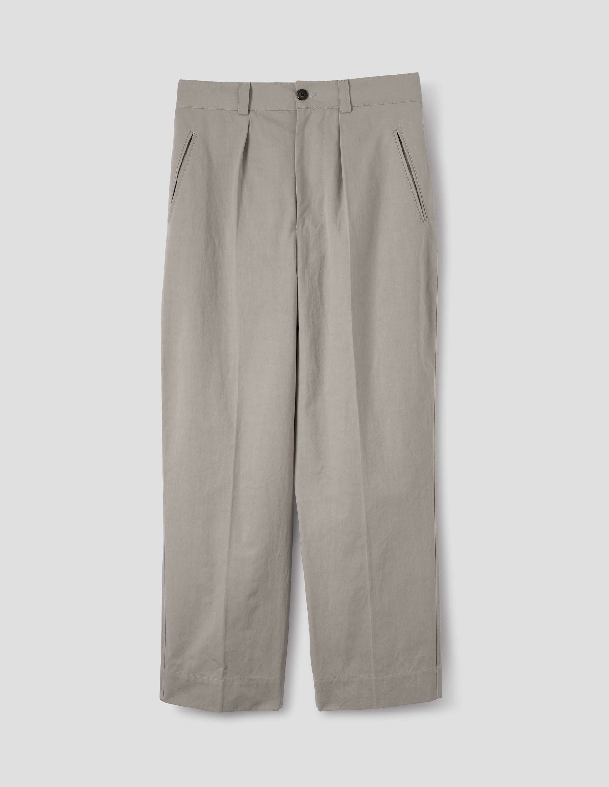 Light grey cotton trousers, with single pleats, horn button closure, slant jet pockets and belt loops. Front flat lay view.