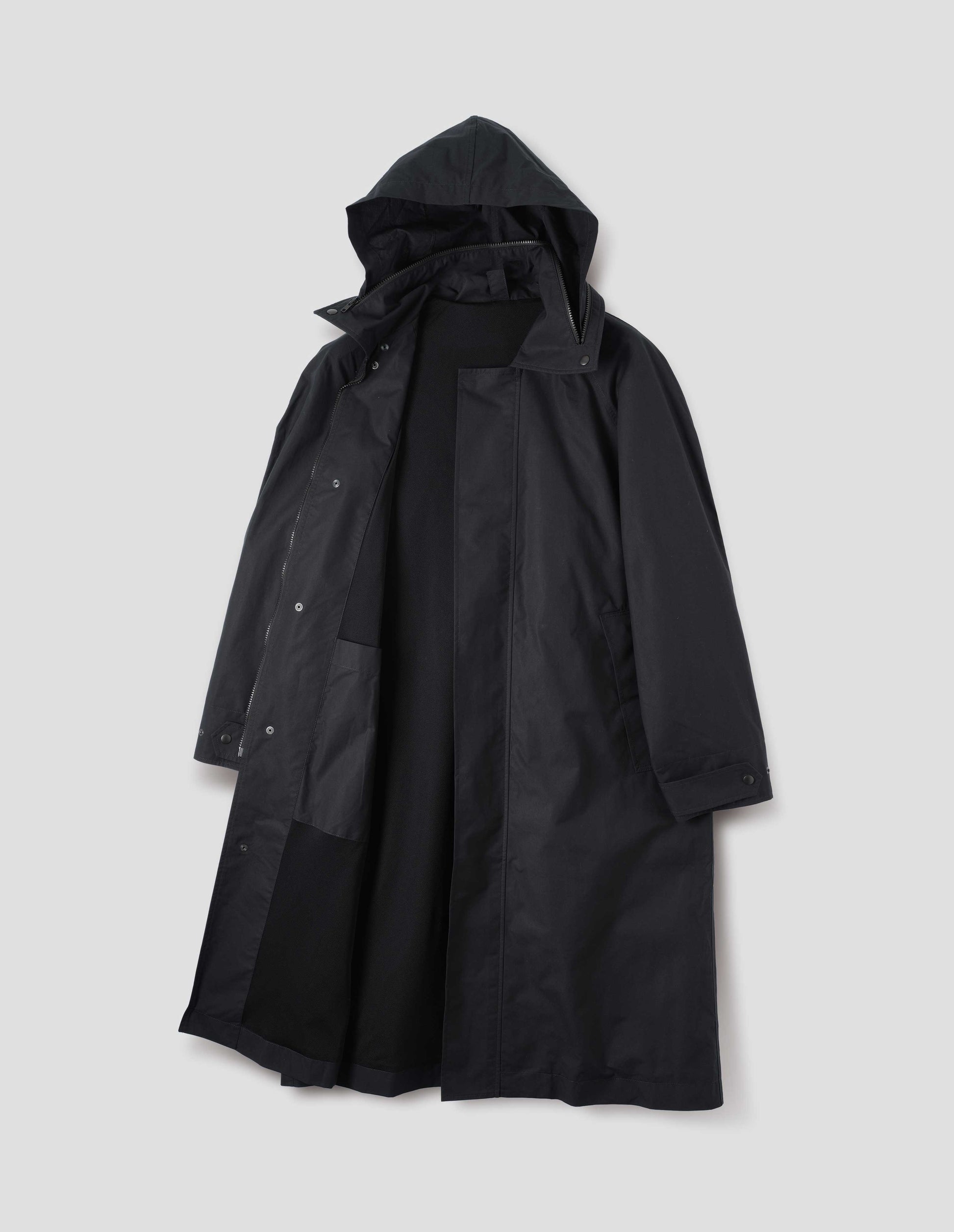 Black ventile cotton poplin longline mac with slant pockets, adjustable popper cuffs and packable hood with internal patch pocket and packable hood. Front flat lay open view. 