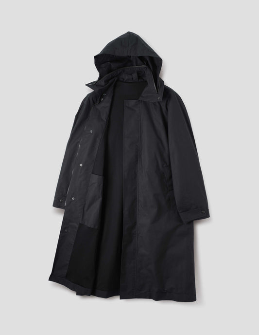 Black ventile cotton poplin longline mac with slant pockets, adjustable popper cuffs and packable hood with internal patch pocket and packable hood. Front flat lay open view. 