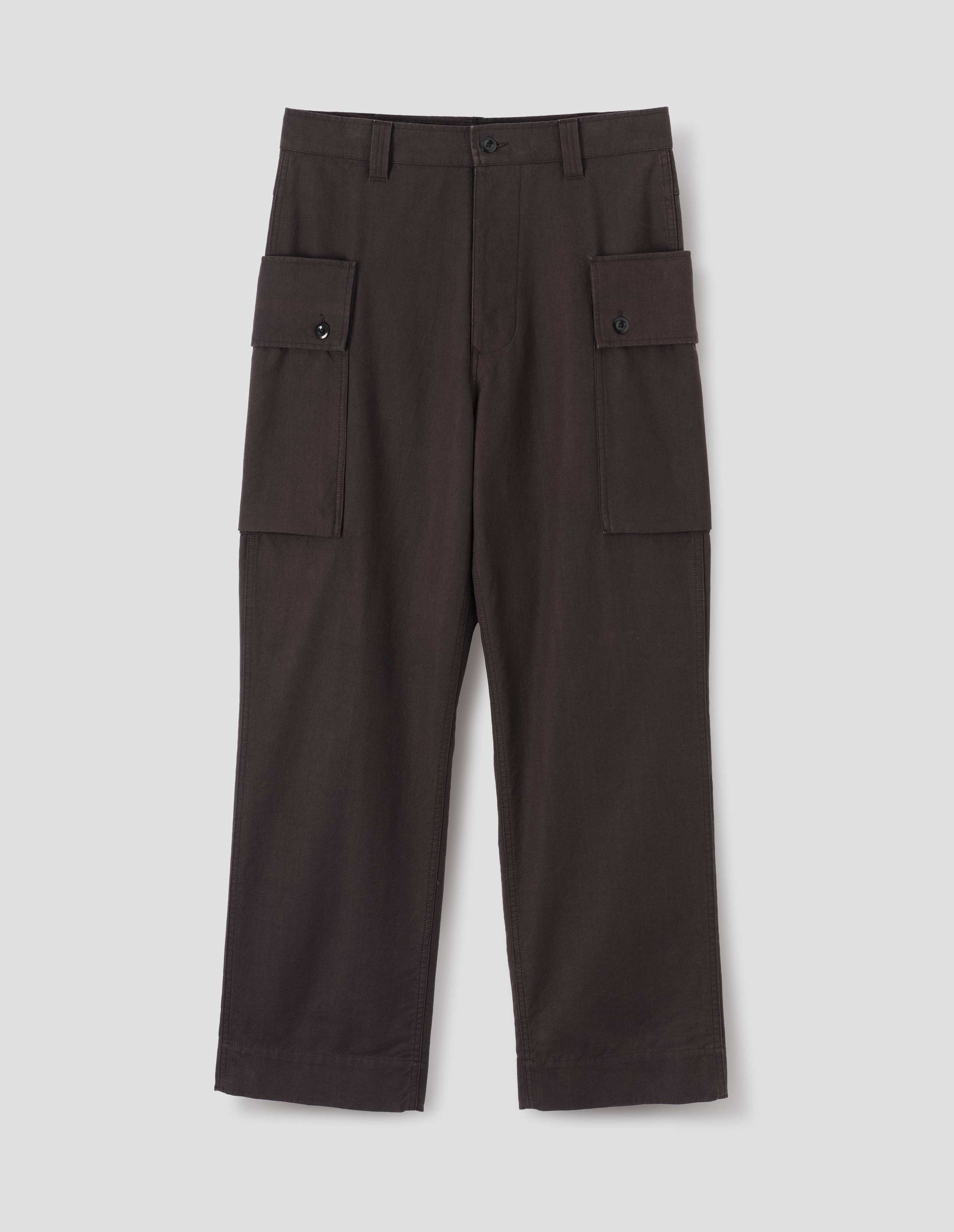 Dark brown cotton drill cargo trousers with deep flap button fastening patch pocket, concealed hand pockets and belt loops. Front flat lay view.