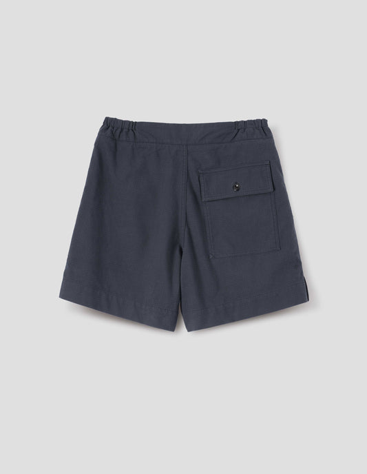 Dark blue shorts with side-elasticated waistband, corozo brace button-through back flap patch pocket and side split hem. Back flat lay view.