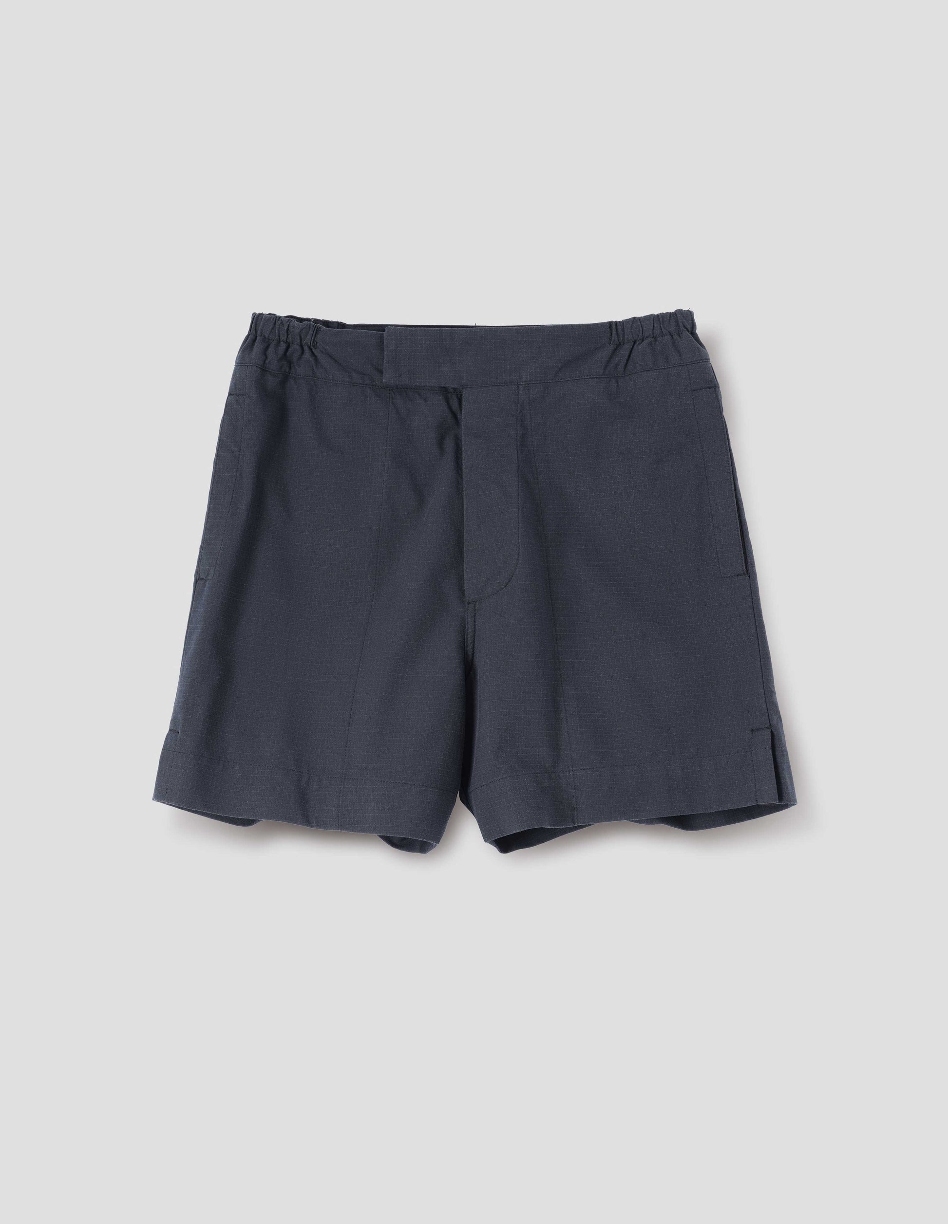 Dark blue shorts with side-elasticated waistband, concealed hook and bar tab fastening and corozo brace button fly and side split hem. Front flat lay view.
