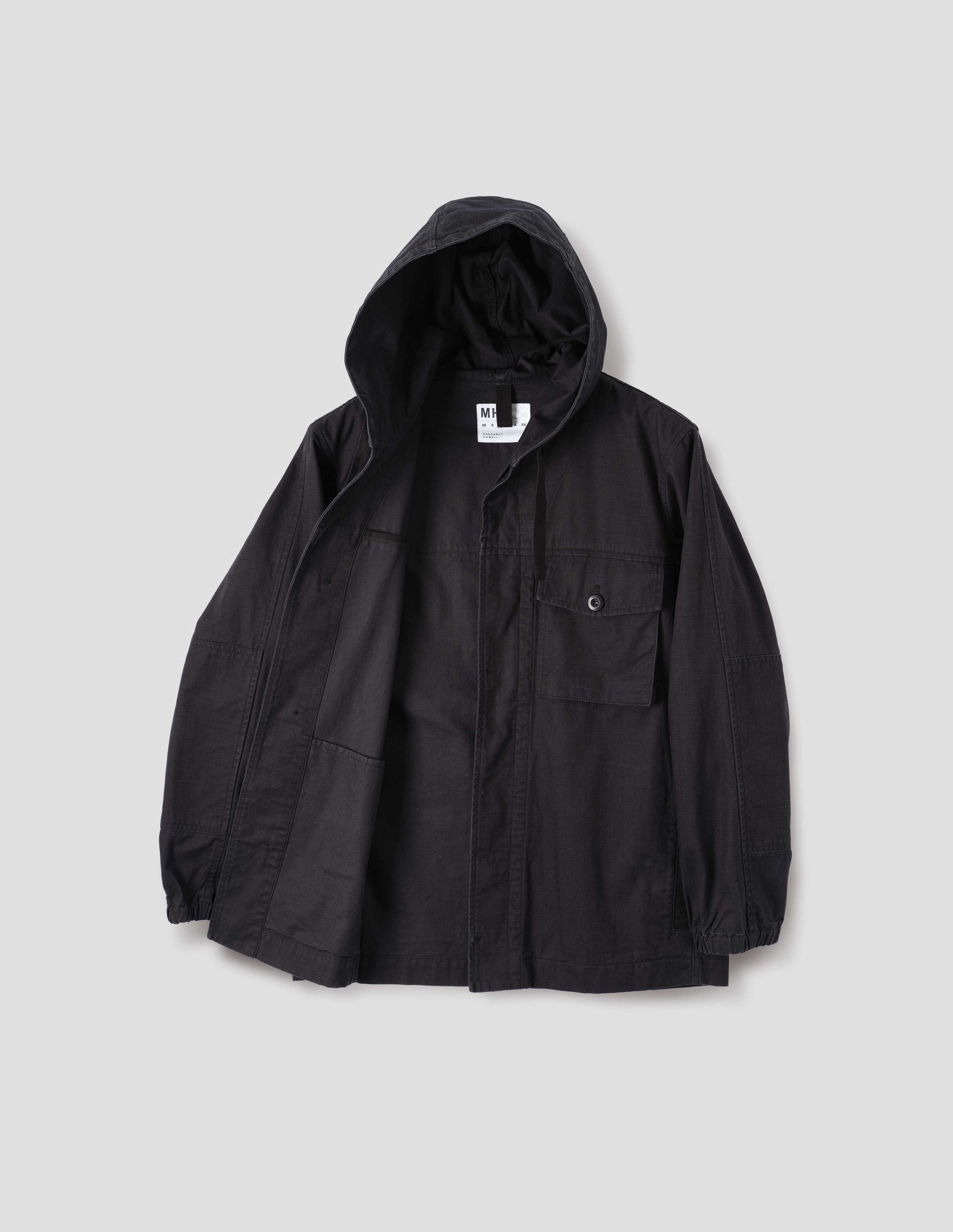 Indigo blue twill hooded jacket, with flap patch chest pocket, concealed placket, drawcord adjustable hood, elasticated cuffs and hanger loop on inside collar. Front flat lay open view.