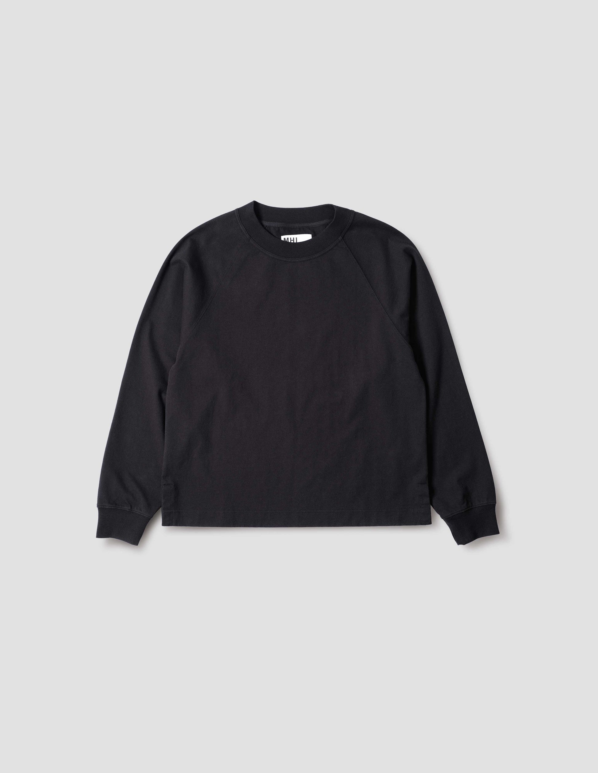 Black cotton long sleeve t-shirt with raglan sleeve, single rib trims on neck and cuffs and vent split hem. Front flat lay view.