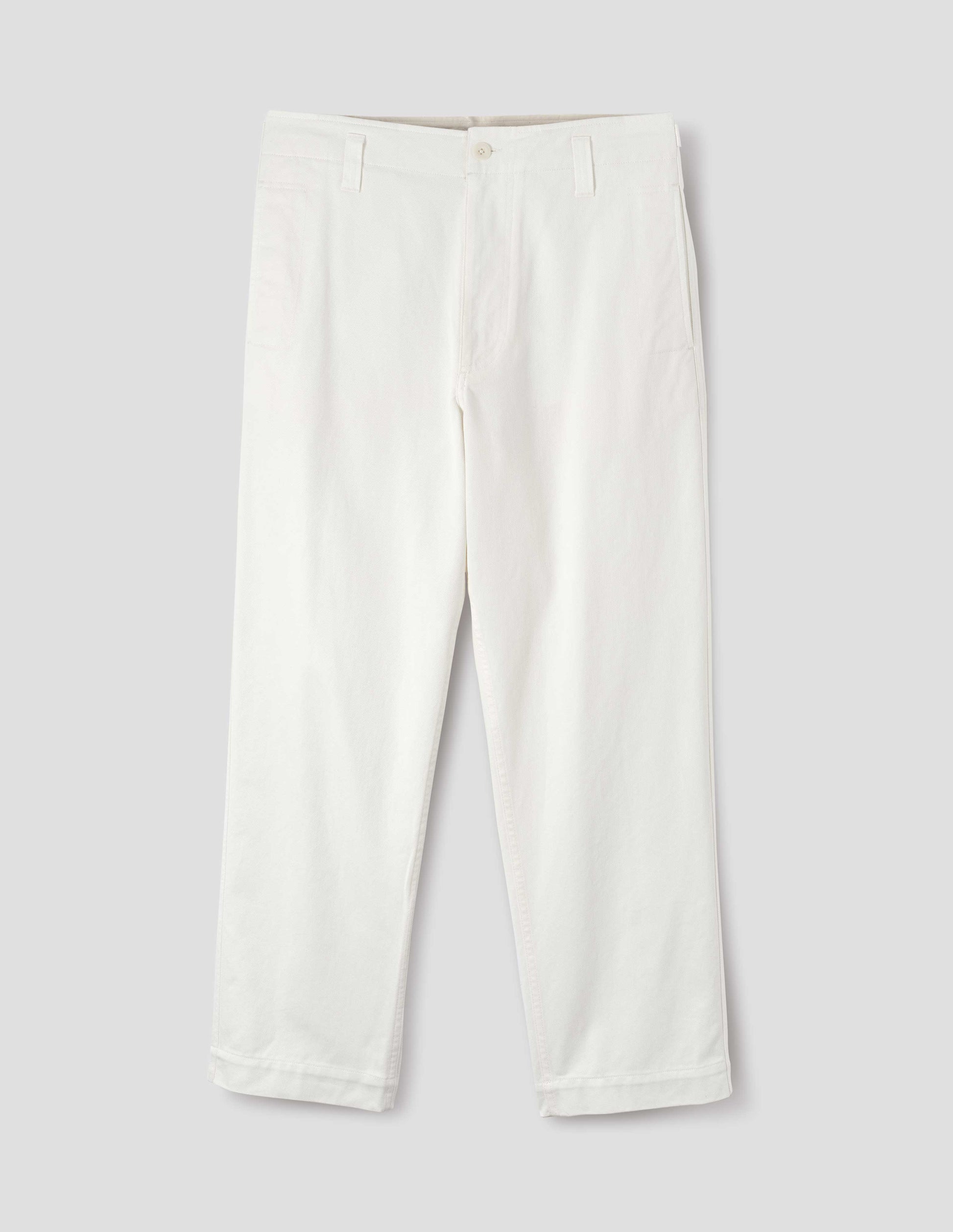 White cotton drill trousers with belt loops, slant side pockets and corozo button fastening. Front flat lay view.