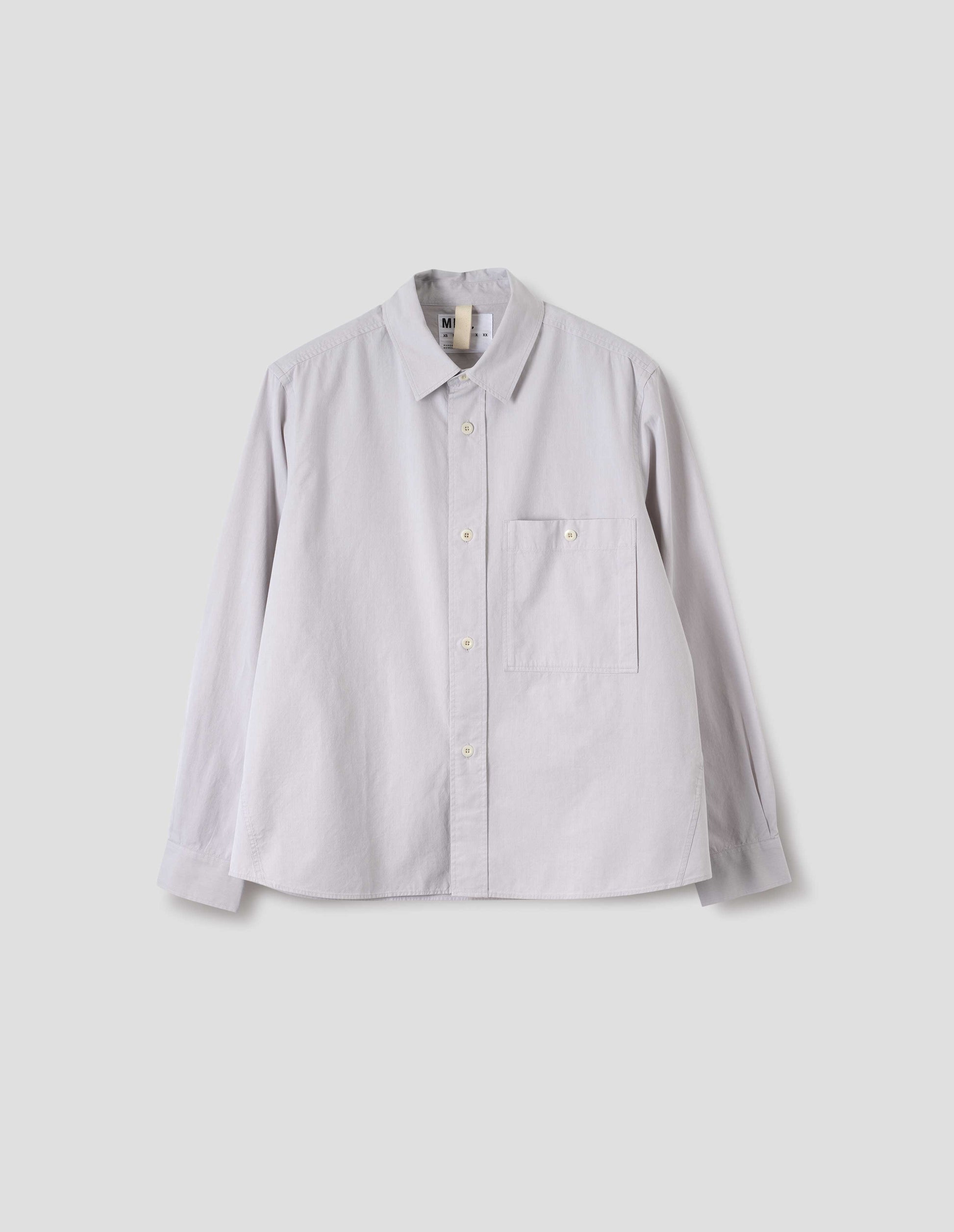 Light grey cotton canvas shirt, with raised placket, corozo button fastening, patch pocket on chest and hanger loop detailing on inside collar. Front flat lay view.
