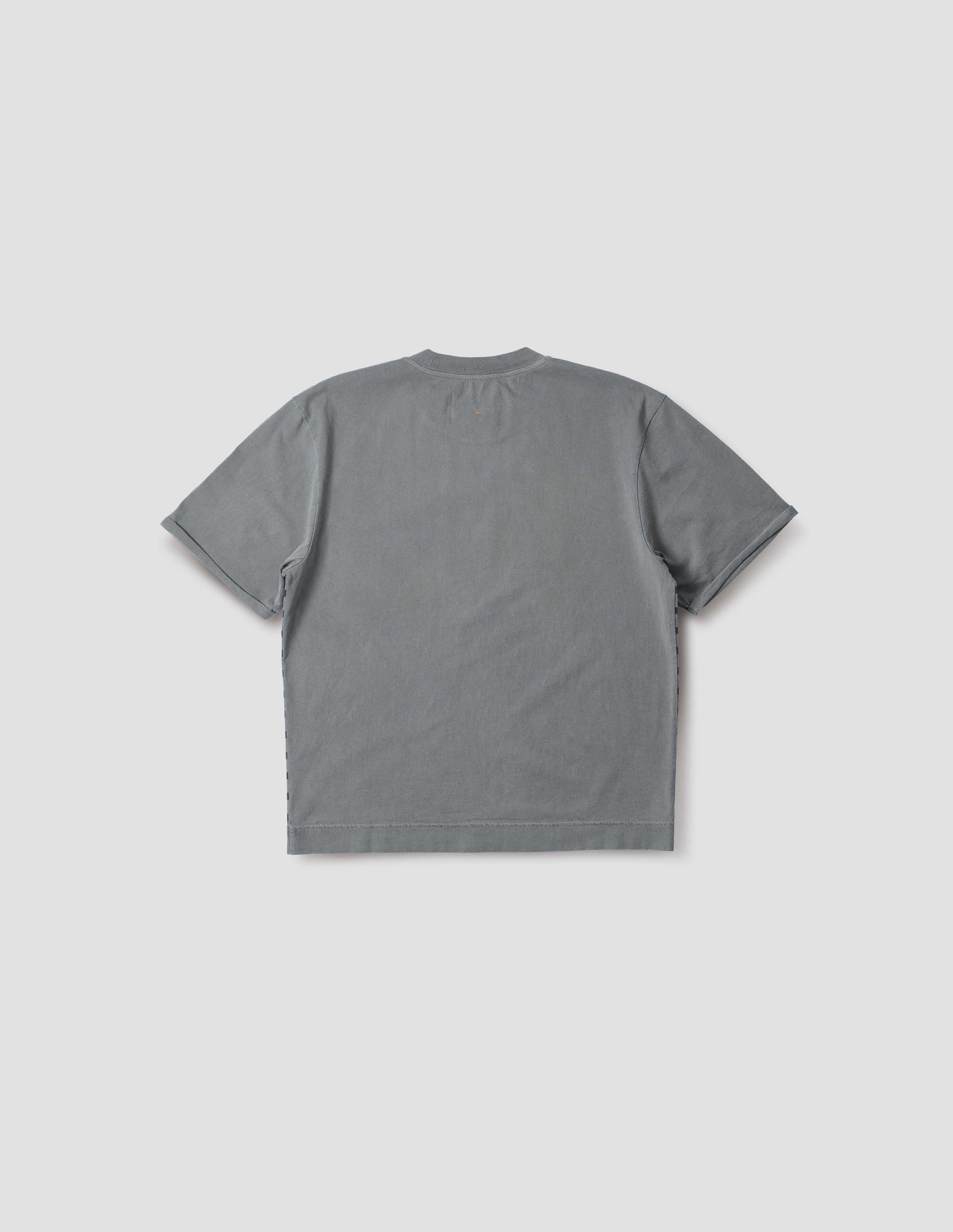 Blueish grey short sleeve t shirt with flatlock stitch detailing and rolled raw sleeve hems with a single bar tack. Back flat lay view.
