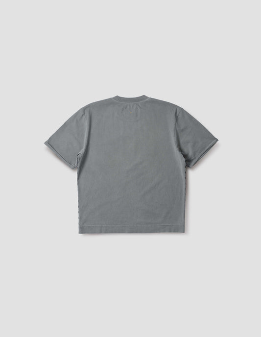 Blueish grey short sleeve t shirt with flatlock stitch detailing and rolled raw sleeve hems with a single bar tack. Back flat lay view.
