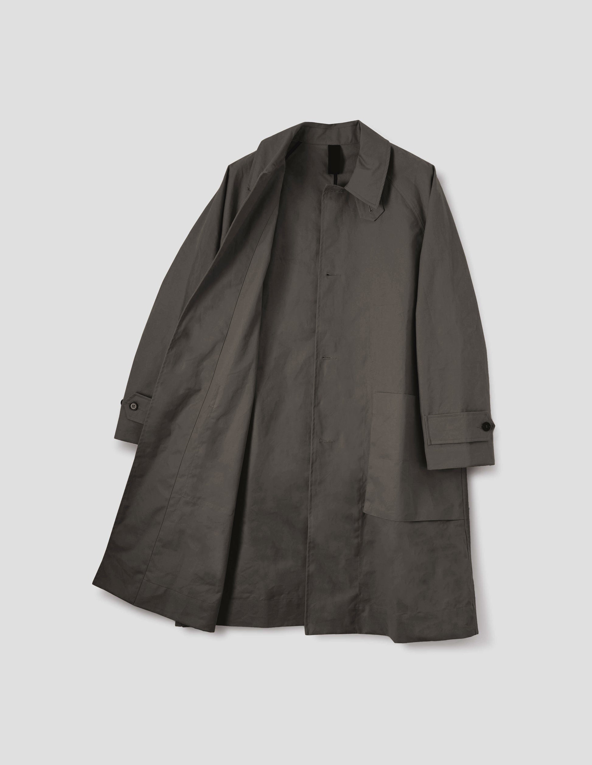 Greyish brown long sleeve cotton mac, with storm tab fastening neck, raglan sleeve, button tab adjustable cuffs and large patch bellow pockets. Front flat lay open view.