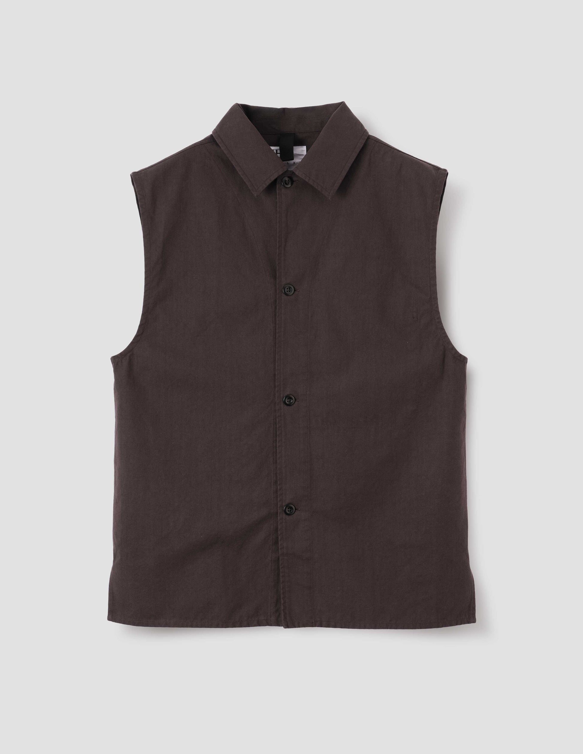Dark brown cotton drill sleeveless overshirt with corozo button fastening, hanger loop on inside of collar and vent split hem. Front flat lay view.