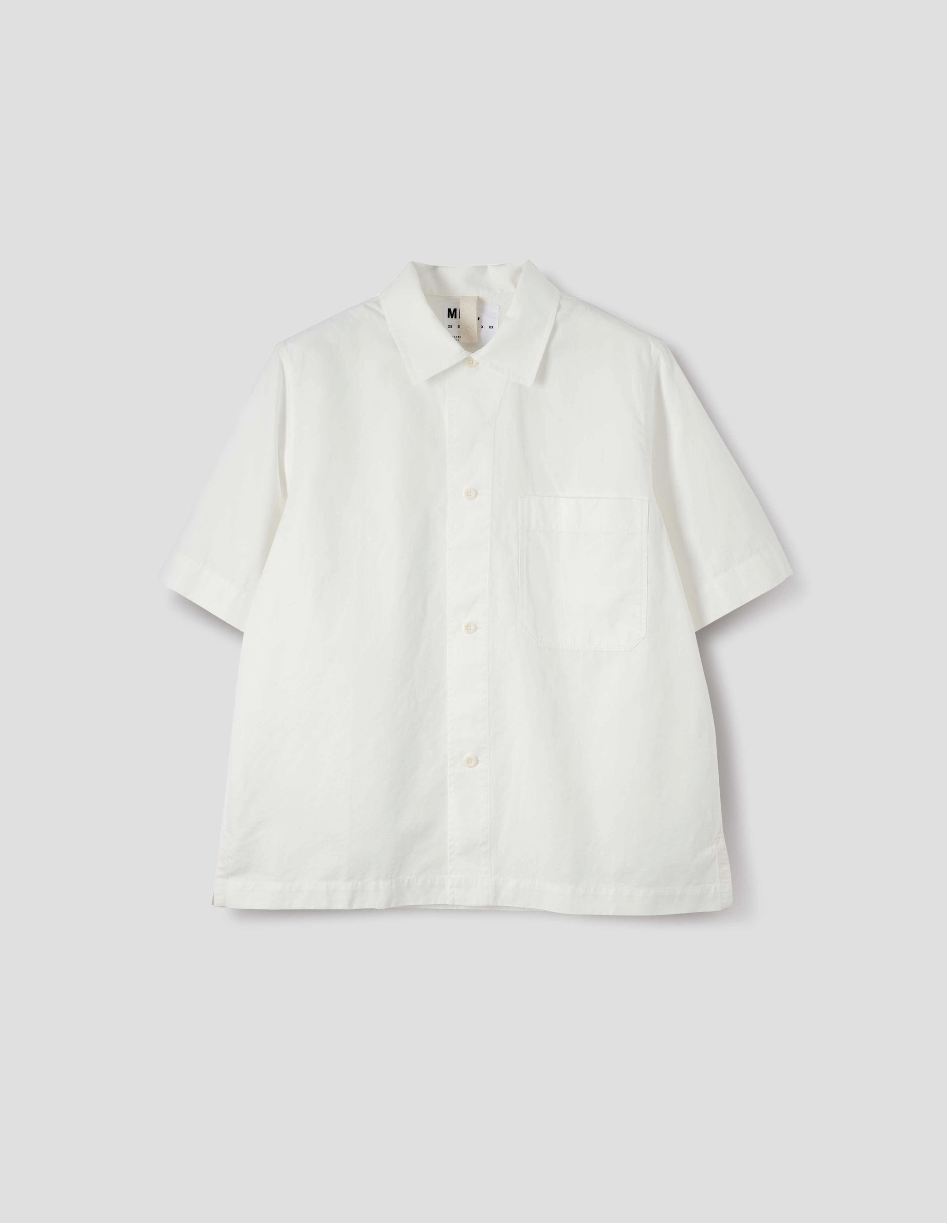 White cotton and linen short sleeve shirt, with large patch chest pocket, side split hem and corozo brace button closure. Front flat lay view.