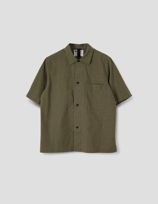 Green cotton short sleeve shirt, with large patch chest pocket, side split hem and corozo brace button closure. Front flat lay view.
