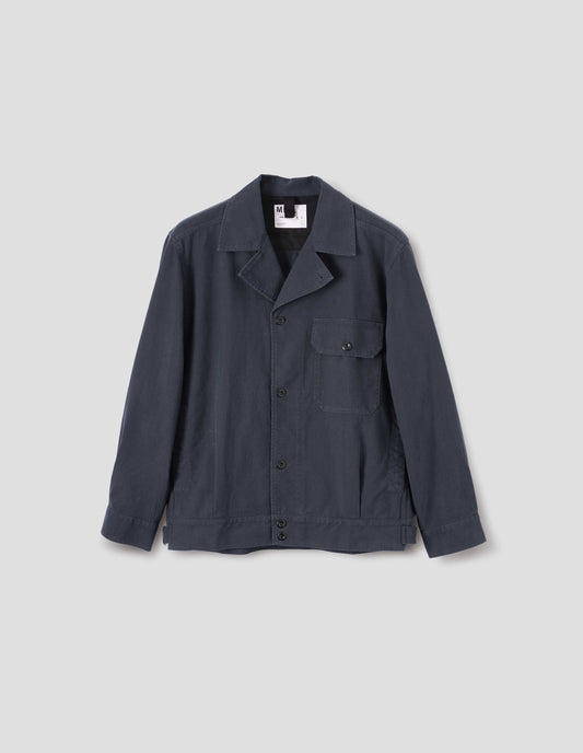 Dark blue jacket with corozo brace button fastening lapel, chest flap pocket, concealed side entry pockets and shirt cuffs, small pleats at hem and side adjustors. Front flat lay view.