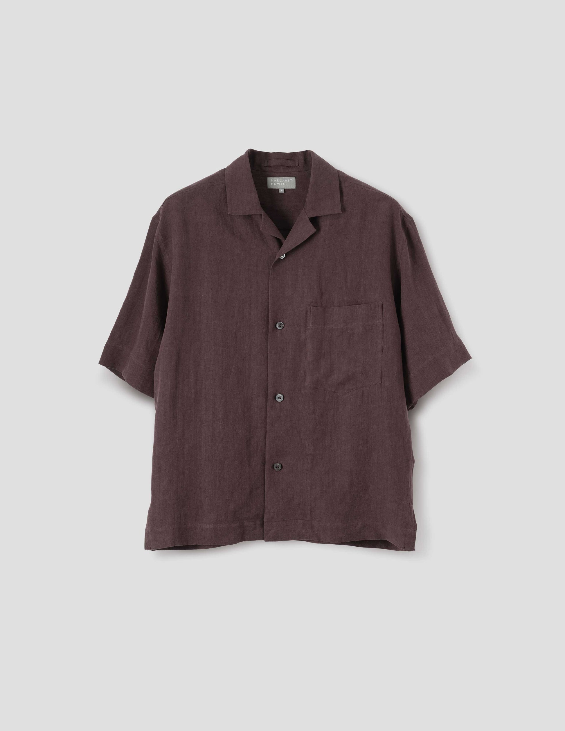 Brown short-sleeve shirt with revere collar, mother of pearl buttons, chest patch pocket and side split hem. Front flat lay view.
