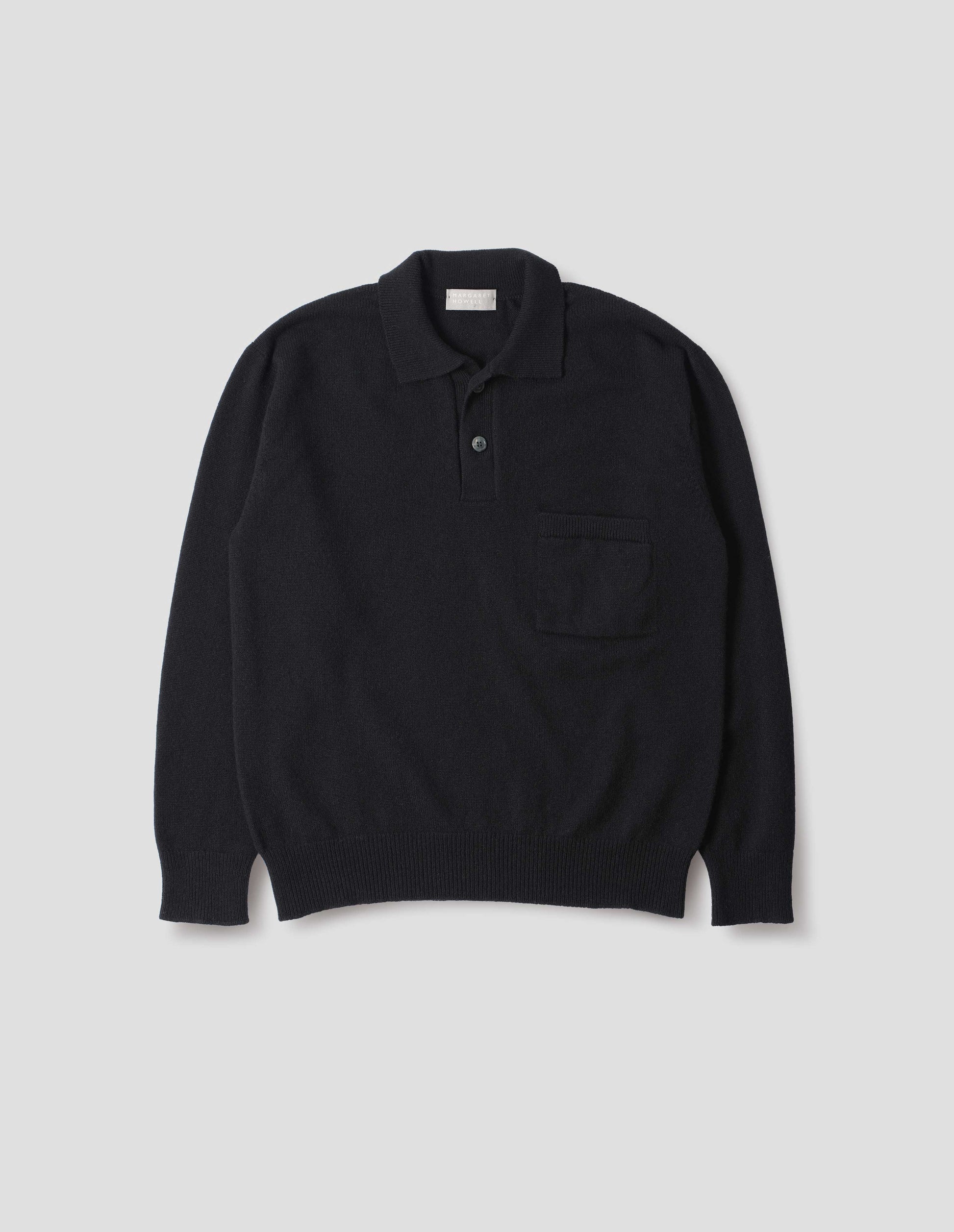 Black merino cashmere polo shirt with dropped sleeve, integral chest pocket, horn button closure and rib collar, cuffs and hem. Front flat lay view.