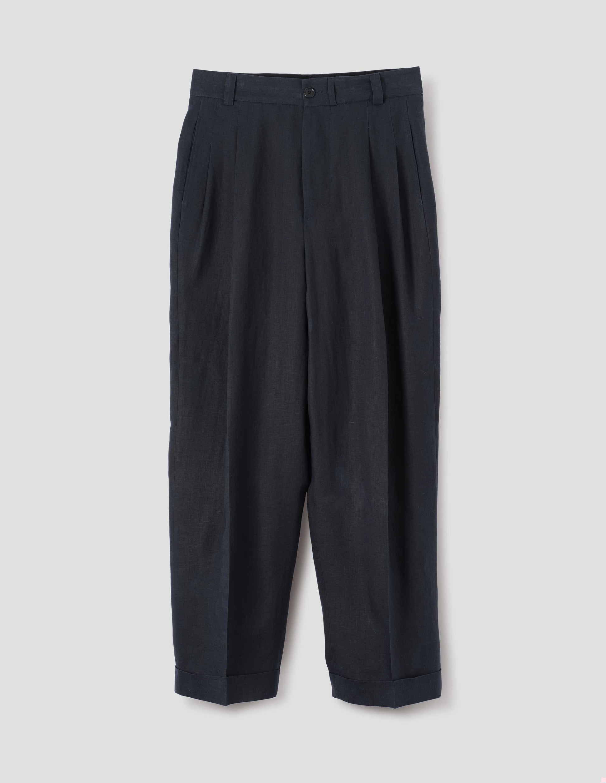 Dark navy trousers, relaxed double pleat with horn button waistband, belt loops and cuffed hem. Front flat lay view.