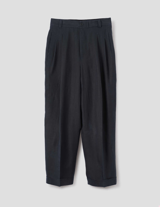 Dark navy trousers, relaxed double pleat with horn button waistband, belt loops and cuffed hem. Front flat lay view.