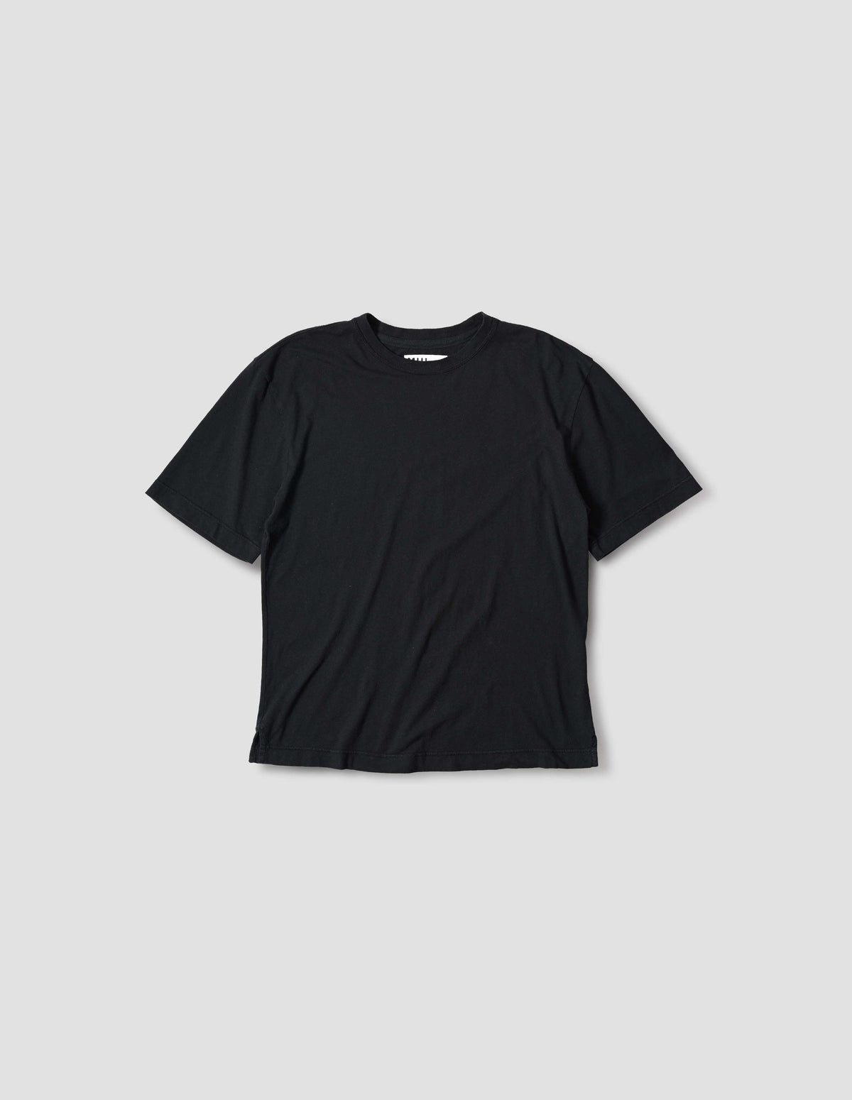 Black t-shirt with herringbone tape detailing on inside neck and vent split hem. Front flat lay view.