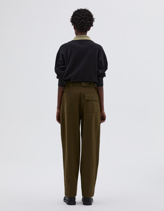 Full body image, back view of model wearing green cotton wool trousers with self waistband with cinch back and belt loops, button through flap patch and patch back pockets. Styled with black long sleeve polo with contrast collar tucked in and black leather boots.
