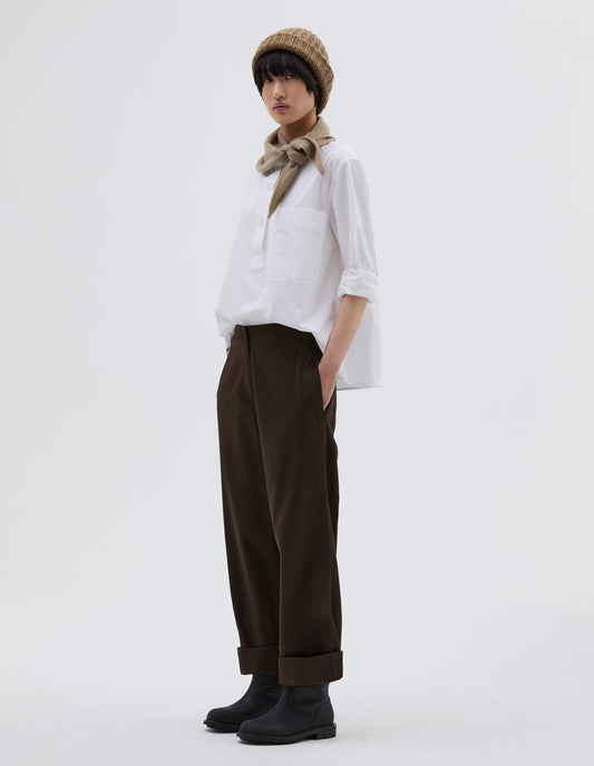 Full body image, side view of model wearing dark brown cotton trousers with zip fly with button through fastening, stitch through waistband, and concealed side pockets. Styled with white shirt tucked in, beige beanie hat, beige knitted scout scarf and black leather boots.