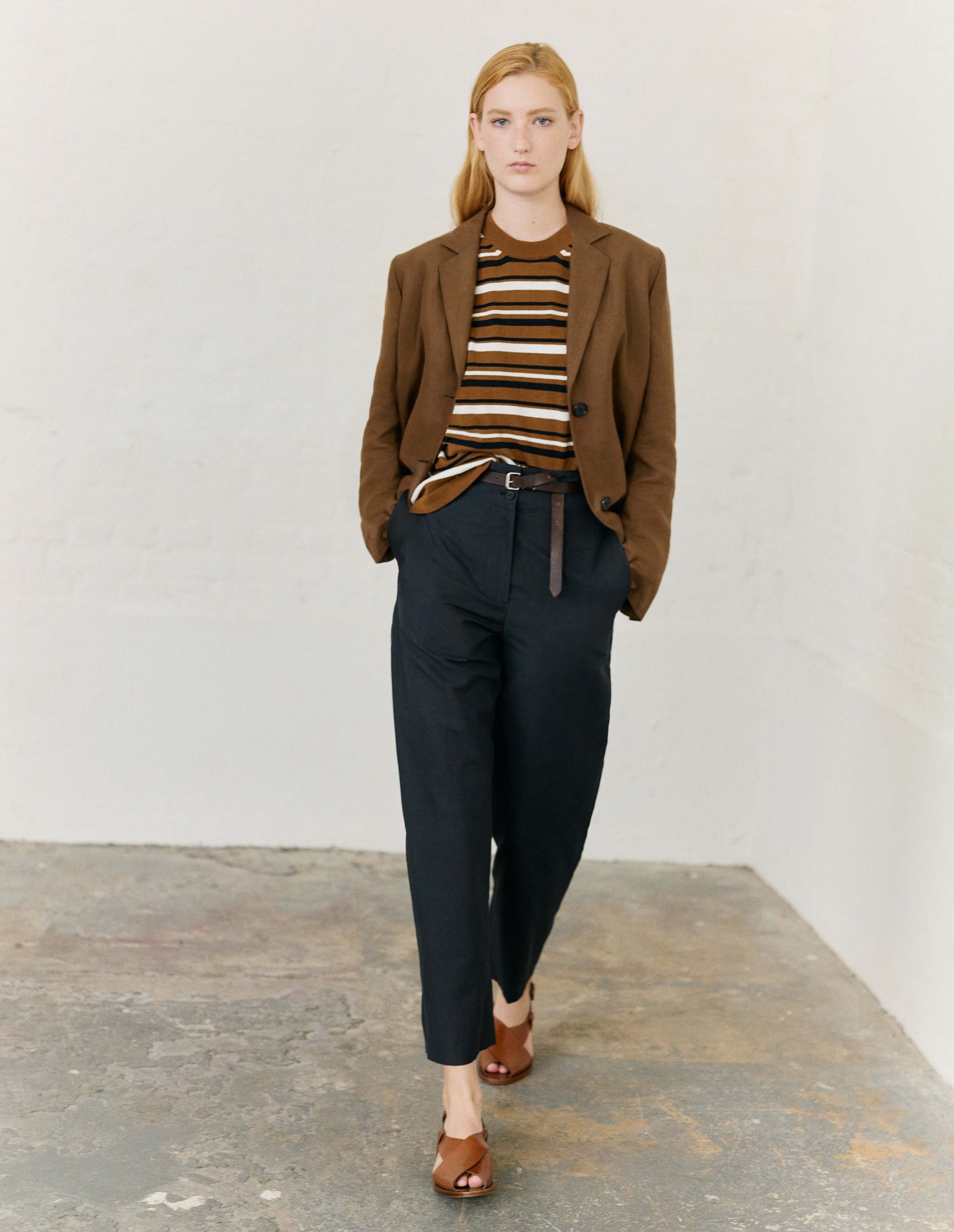 Full body image, front view of model wearing brown, black and off white irregular stripe knitted t-shirt with ribbed round neck. Styled with brown blazer, dark brown leather belt and light brown leather sandals.