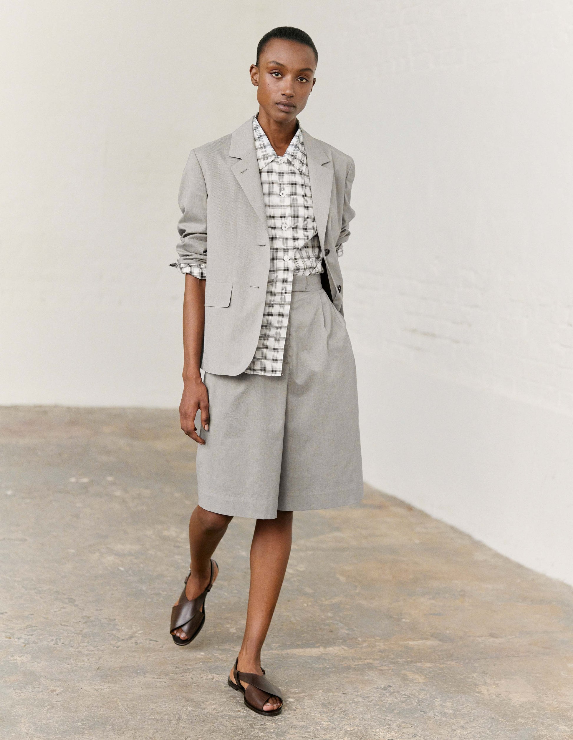 Full body image, front view of model wearing black and cream stripe long shorts with double pleats, hook and bar tab fastening waistband, zip fly and slant side pockets. Styled with black and cream stripe matchng blazer, white with black check shirt  and dark brown leather sandals.