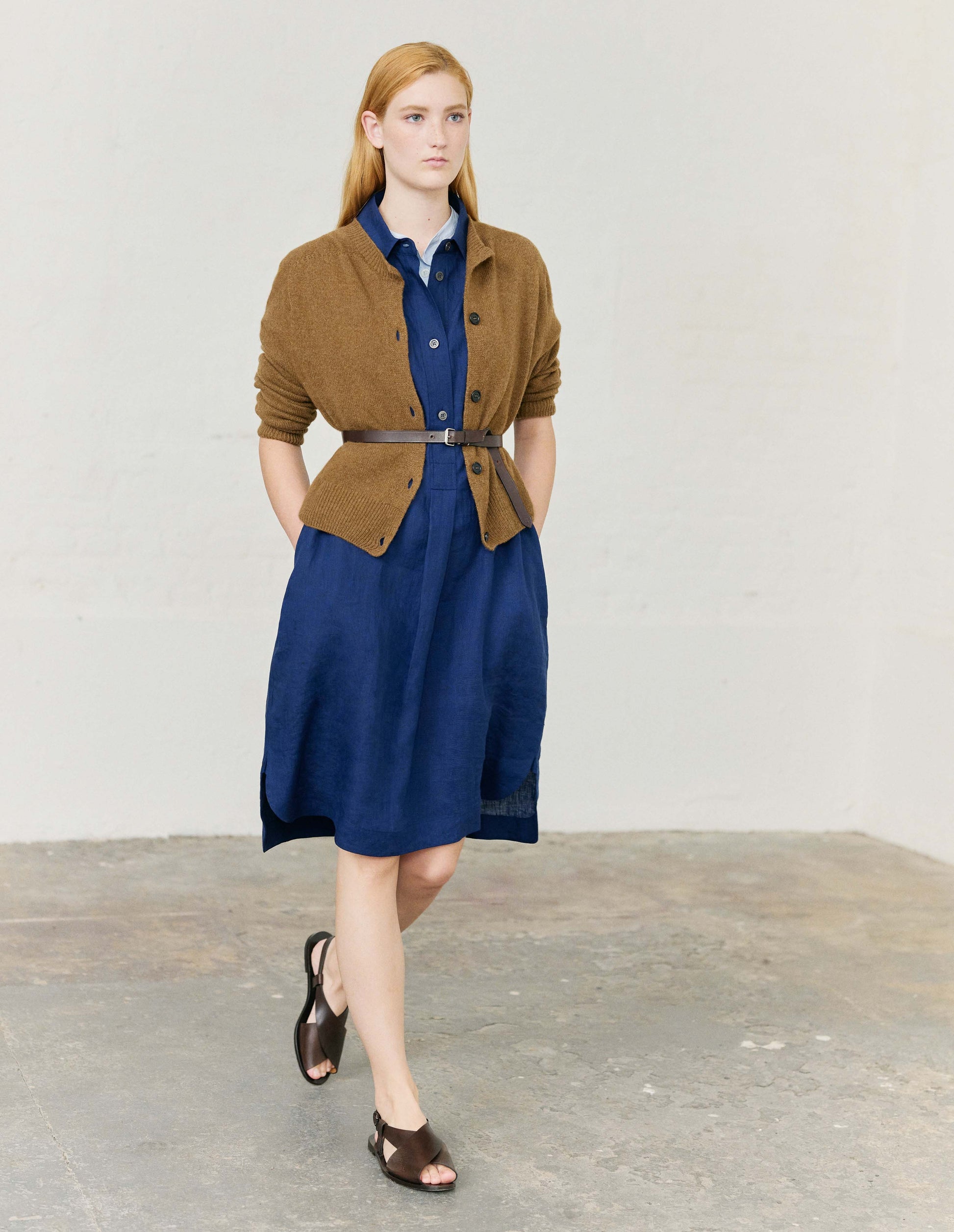 Full body image, front view of model wearing brown long sleeve merino cashmere cardigan with contrast rib neckline, cuffs and hem and dark horn buttons. Styled with light blue shirt, bright blue shirt dress, light brown leather belt and dark brown leather sandals.
