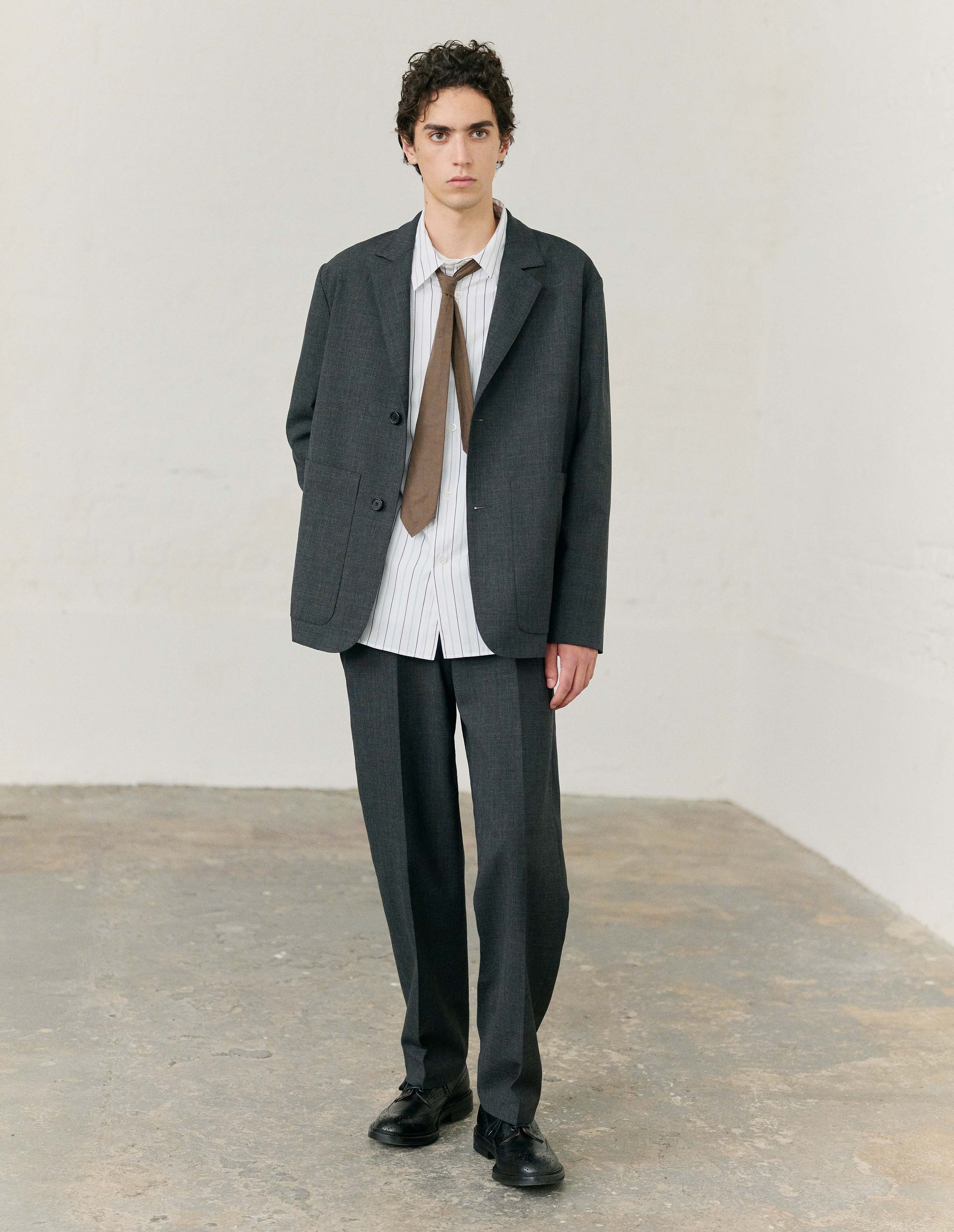 Full body image,front view of model wearing white with grey pin stripe cotton long sleeve shirt, mother of pearl buttons, curved hem and chest patch pocket. Styled with dark grey blazer and matching grey trouers, with black leather shoes. 