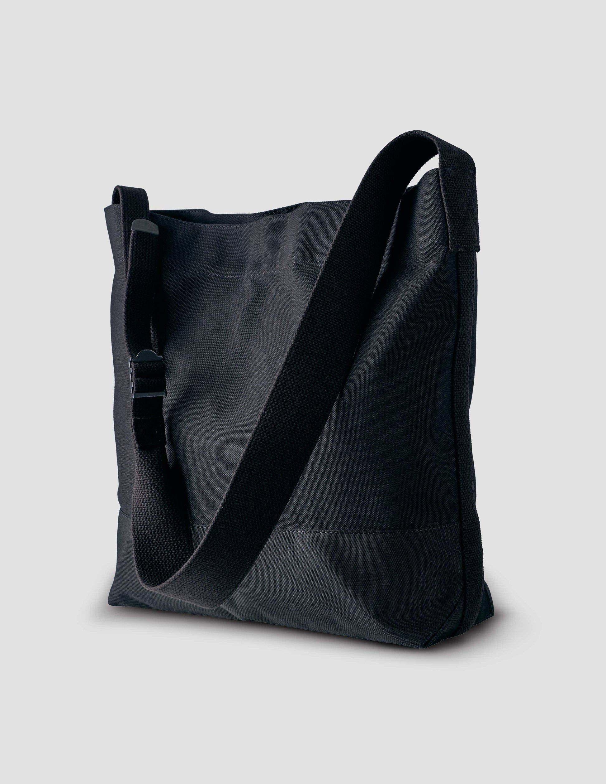 Black heavy cotton canvas shoulder tote bag with adjustable contrast nylon shoulder strap. Front side angle flat lay.