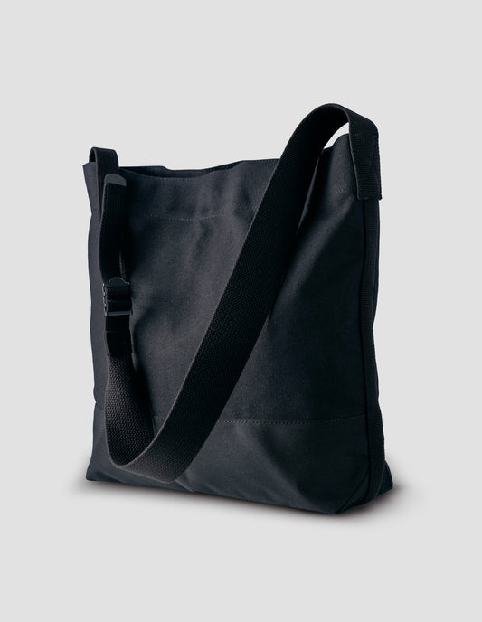 Black heavy cotton canvas shoulder tote bag with adjustable contrast nylon shoulder strap. Front side angle flat lay.