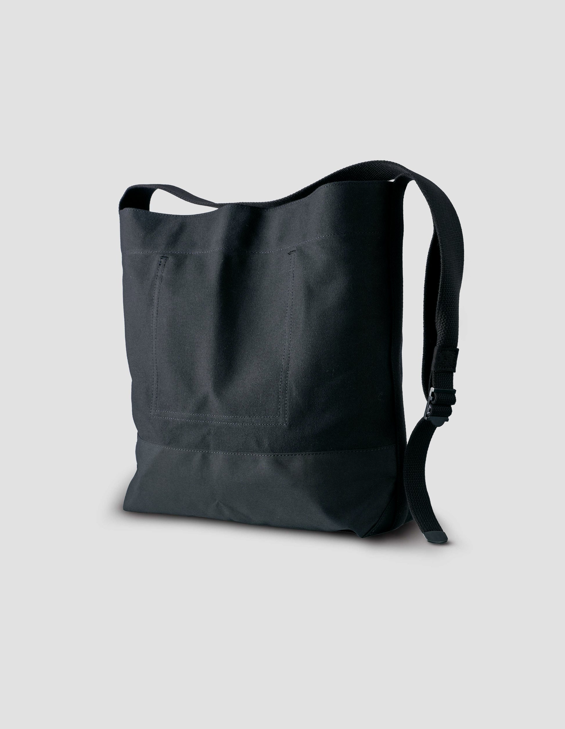 Black heavy cotton canvas shoulder tote bag with adjustable contrast nylon shoulder strap. Back side angle flat lay.