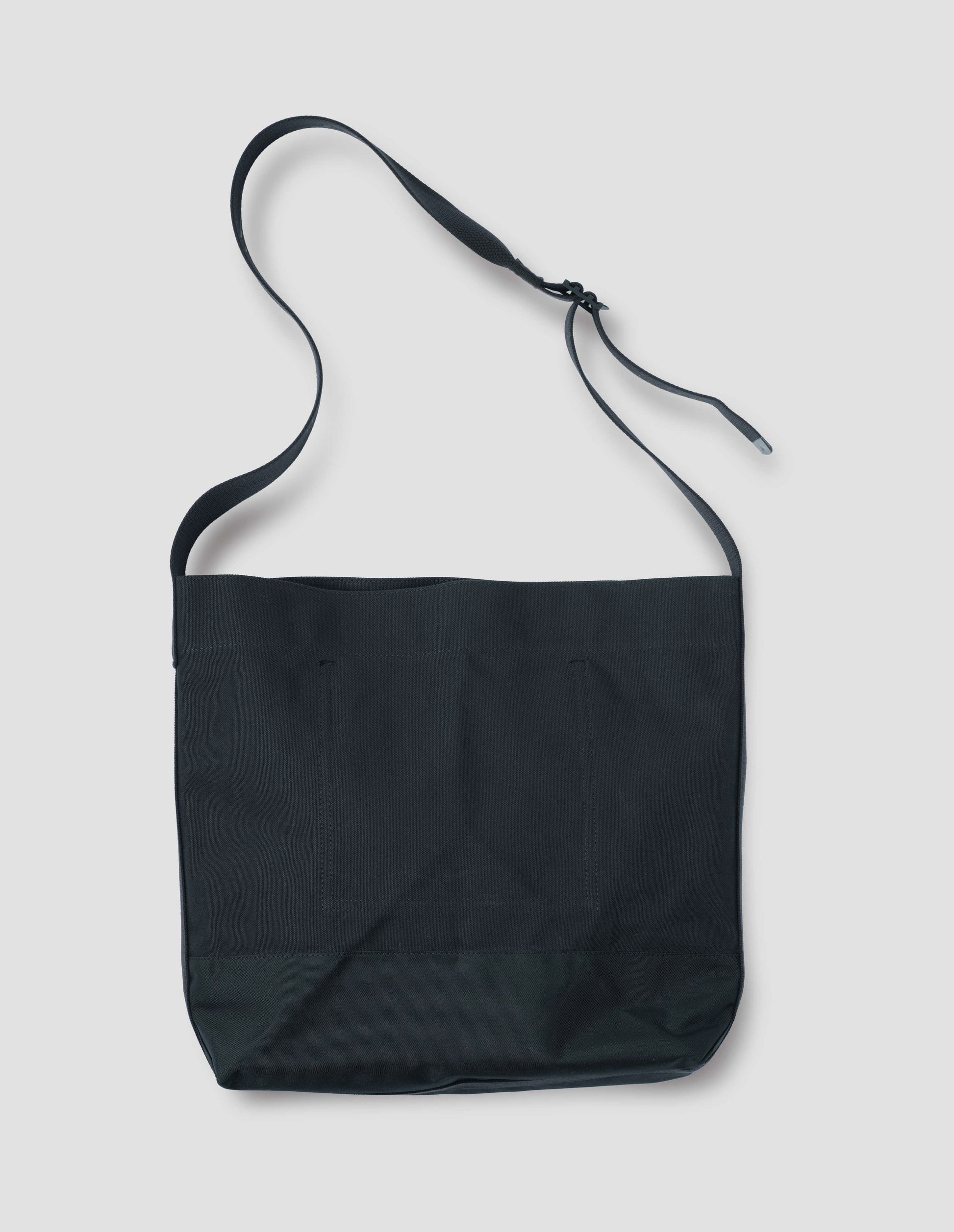 Black heavy cotton canvas shoulder tote bag with adjustable contrast nylon shoulder strap. Back flat lay view.