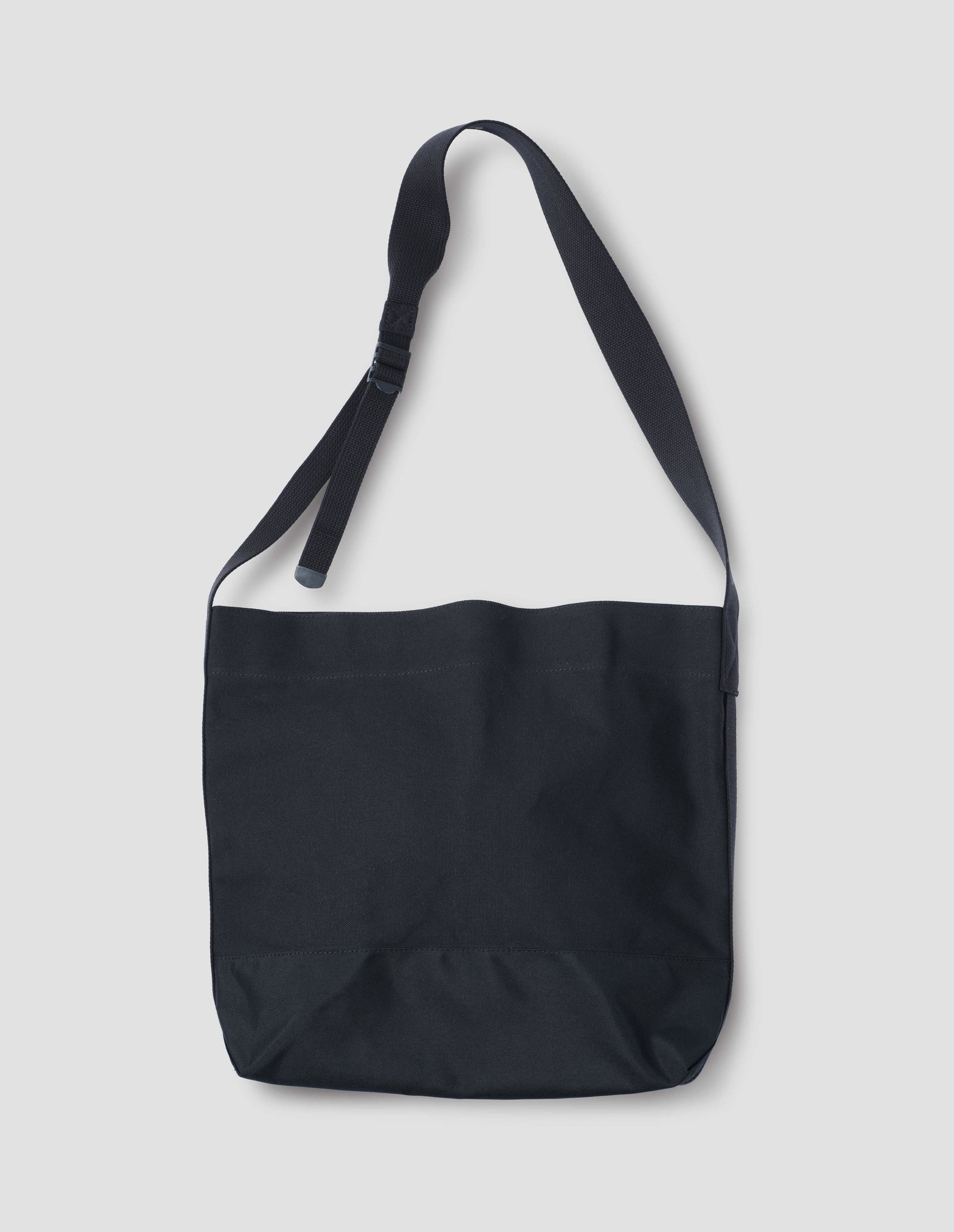 Black heavy cotton canvas shoulder tote bag with adjustable contrast nylon shoulder strap. Front flat lay view.