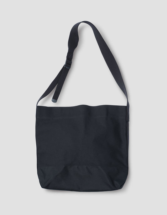 Black heavy cotton canvas shoulder tote bag with adjustable contrast nylon shoulder strap. Front flat lay view.