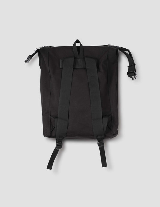 Black cotton canvas rucksack with contrast cotton webbing carry handles, adjustable clip and zip fastening. Back flat lay view.