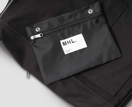 Black cotton canvas rucksack with detachable pocket pouch with zip fastening and white MHL. label logo. Close up detail flat lay.