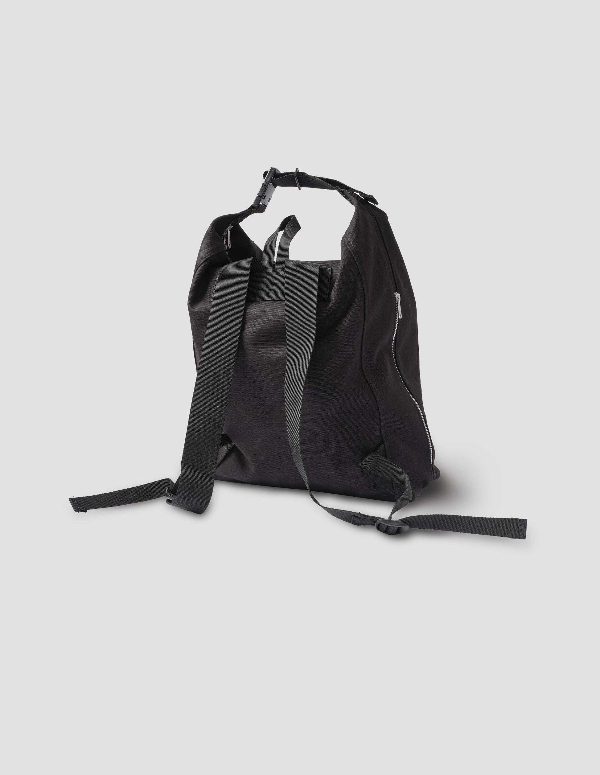 Black cotton canvas rucksack with contrast cotton webbing carry handles, adjustable clip and zip fastening side pockets. Back flat lay view.