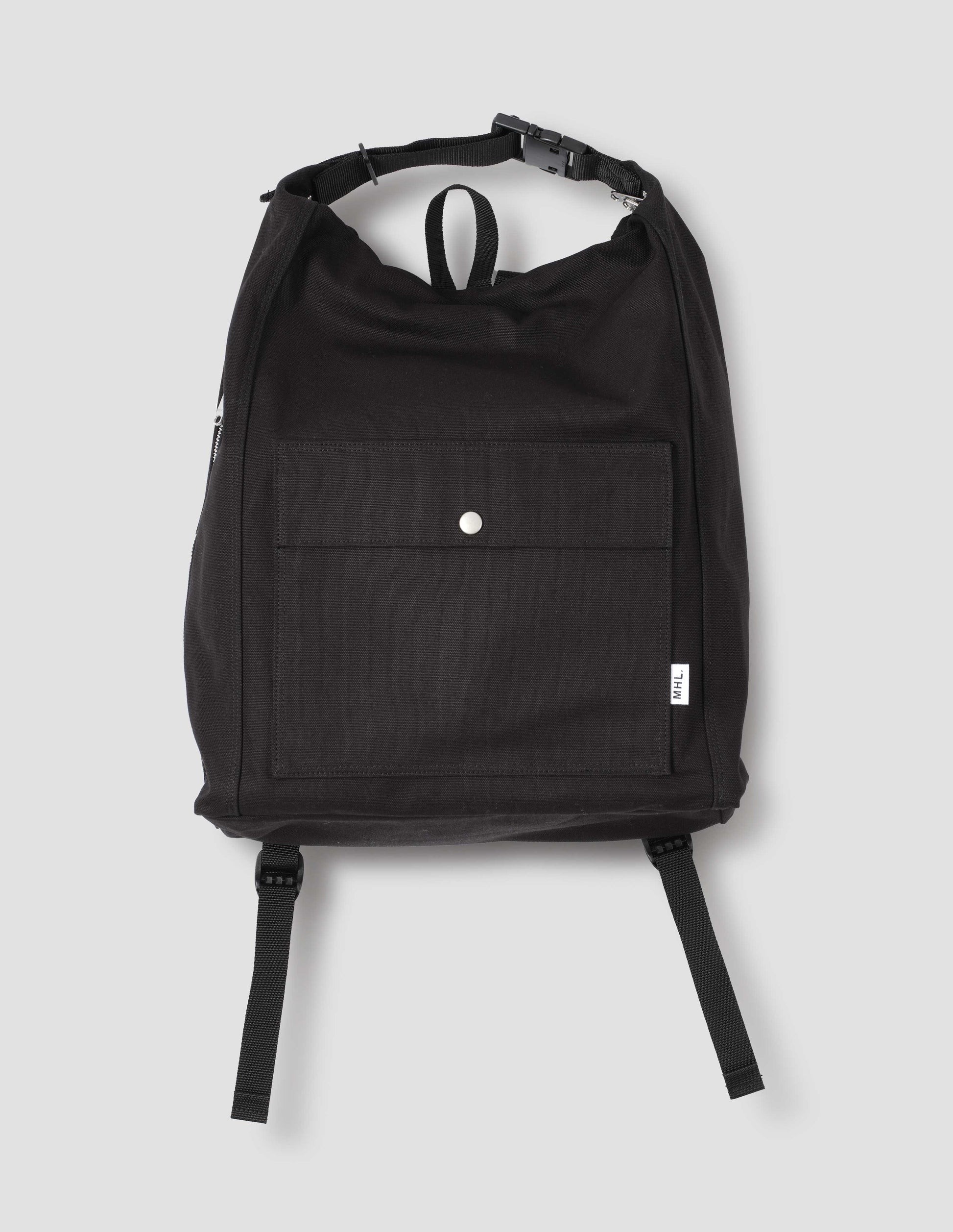 Black cotton canvas rucksack with contrast cotton webbing carry handles, adjustable clip, zip fastening, front pocket with popper closure, and white tag with MHL. logo. Front flat lay view.