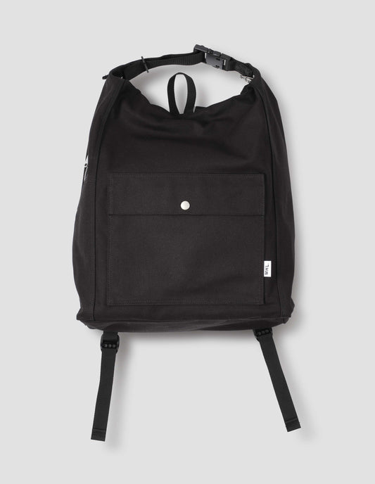 Black cotton canvas rucksack with contrast cotton webbing carry handles, adjustable clip, zip fastening, front pocket with popper closure, and white tag with MHL. logo. Front flat lay view.