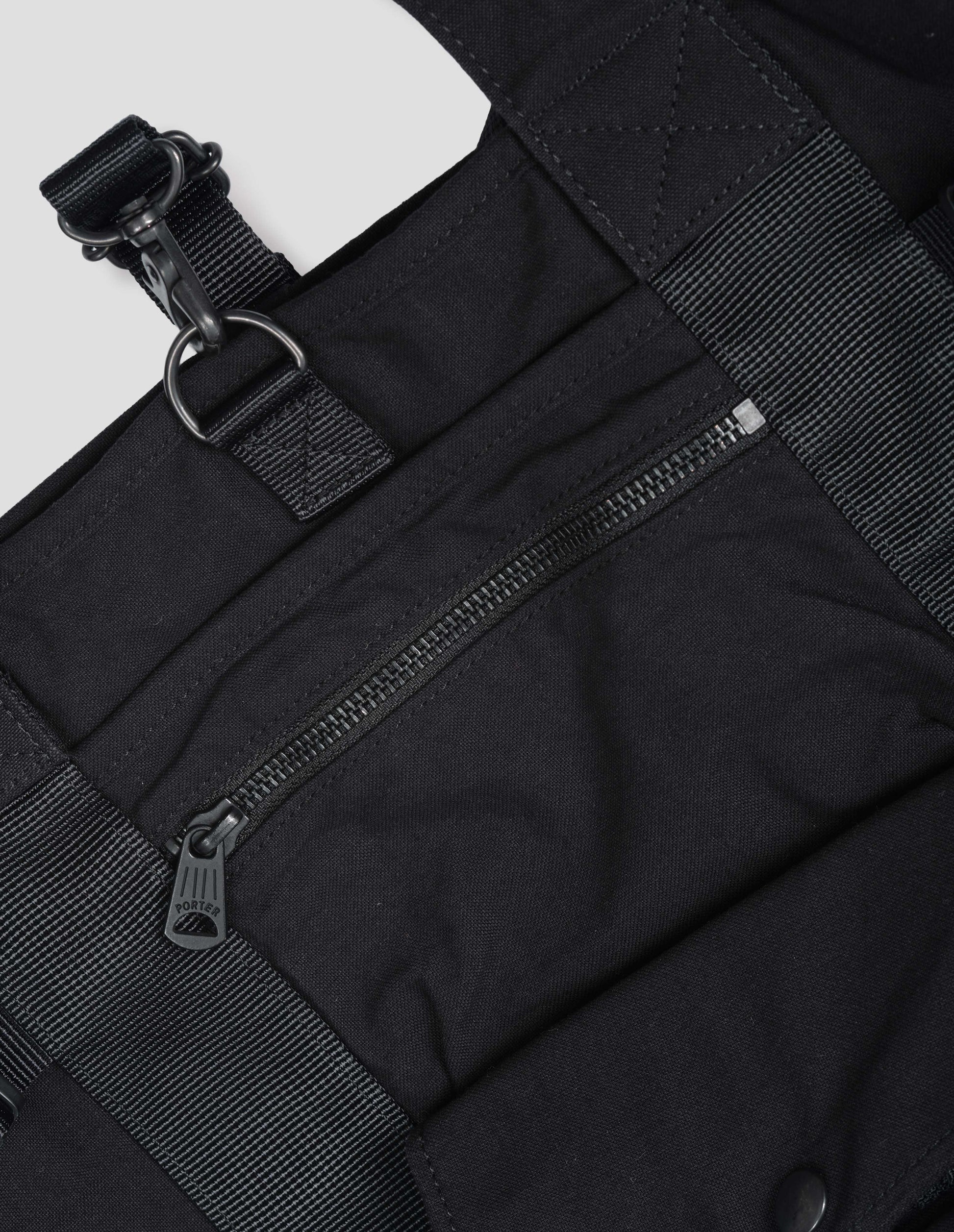 Black backpack with contrast webbing, zip pocket and press stud pocket. Detail flat lay view.
