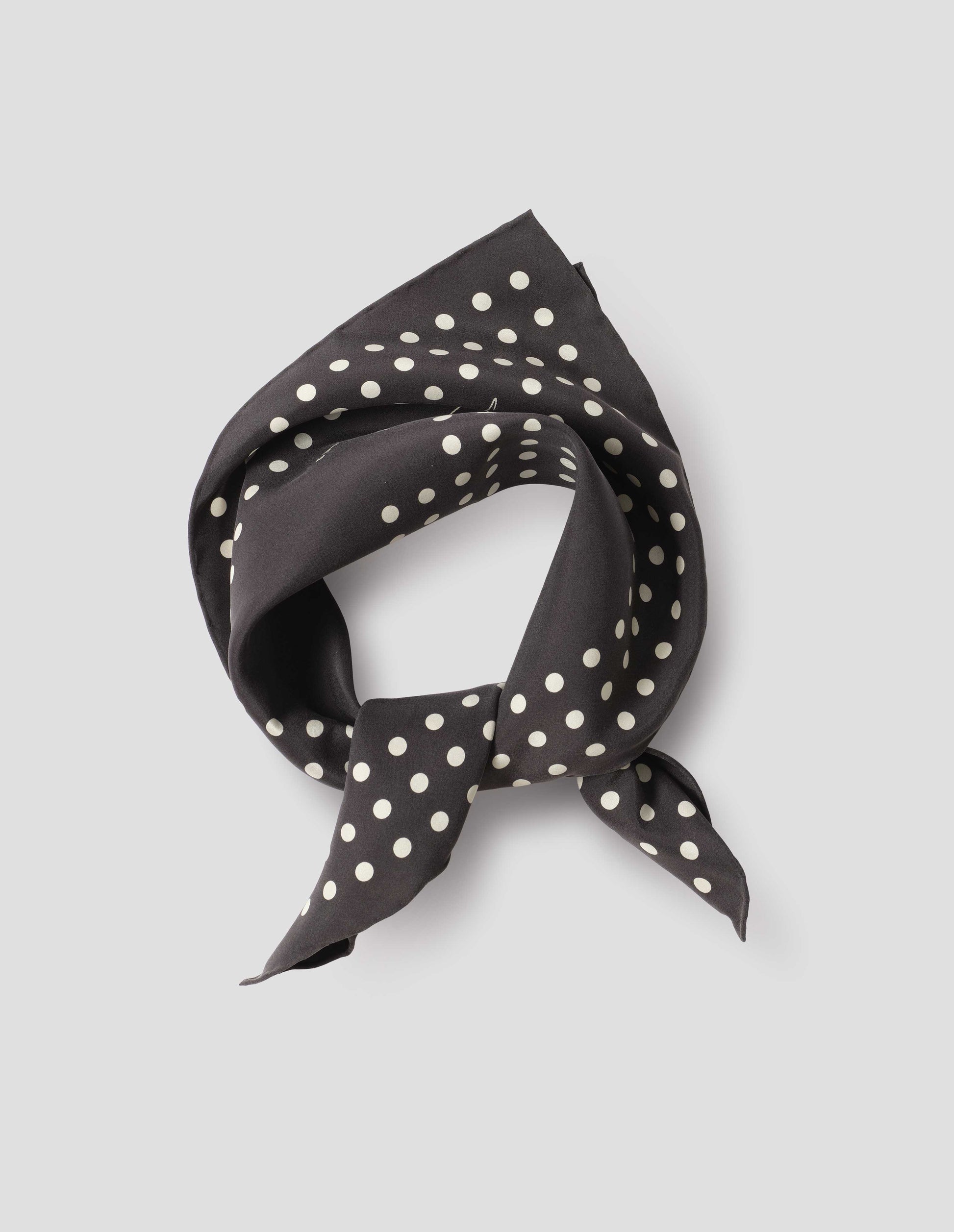 Black folded and tied silk neck scarf with white dots and hand rolled edges. Close up flat lay view.
