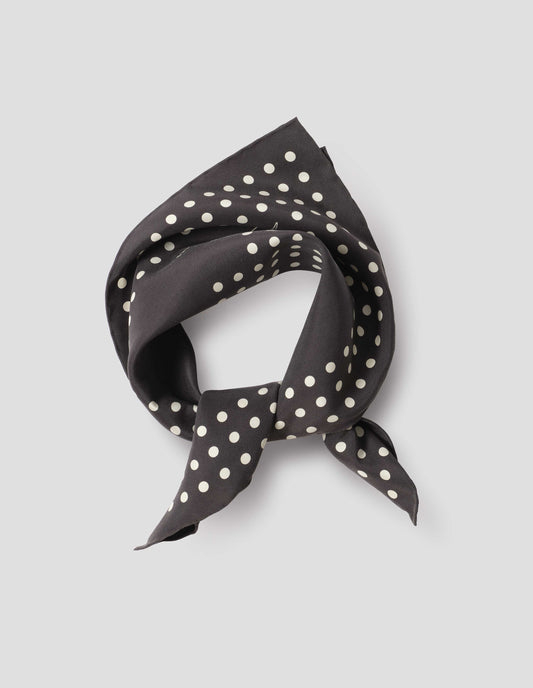 Black folded and tied silk neck scarf with white dots and hand rolled edges. Close up flat lay view.