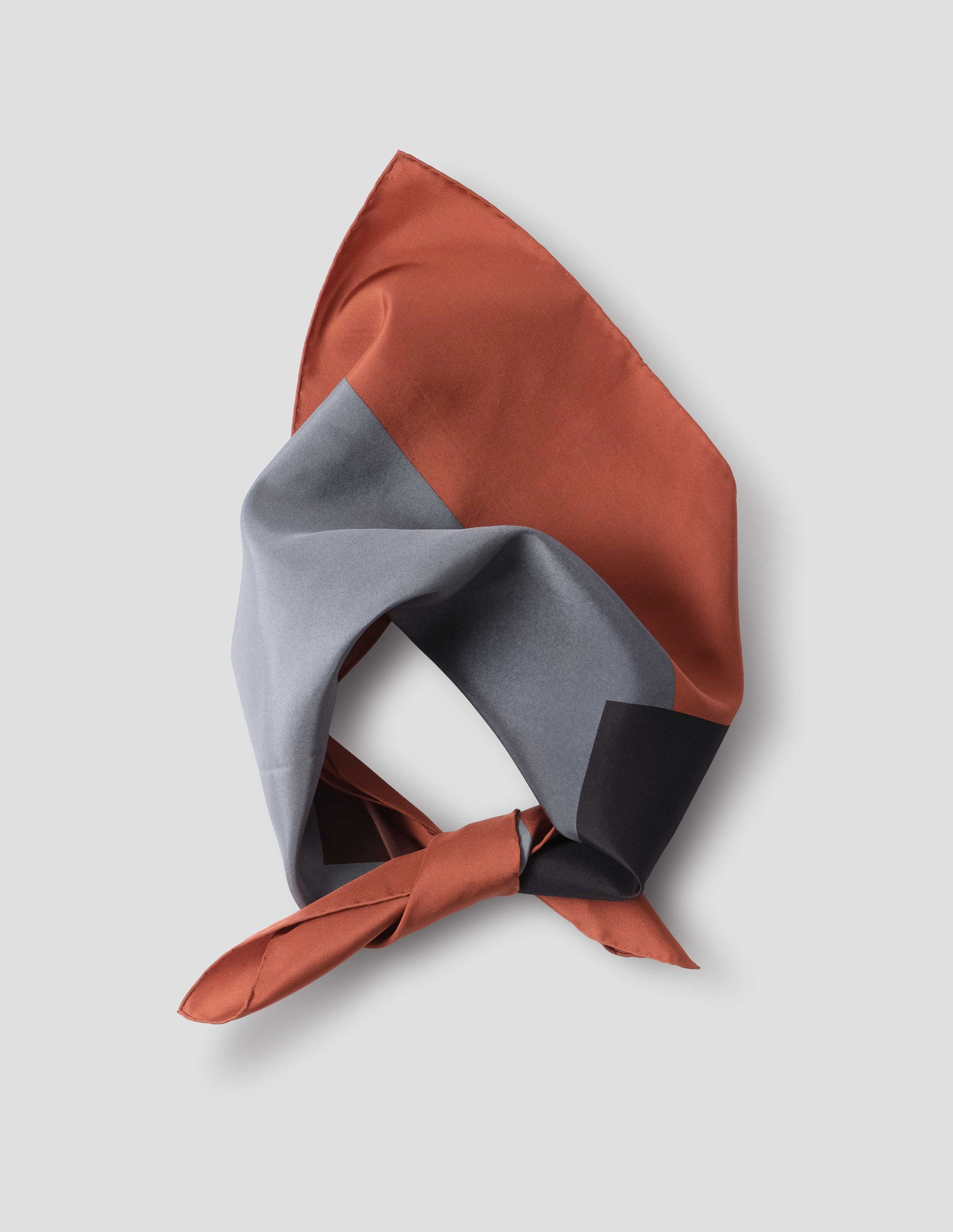 Orange-red folded and tied neck scarf with contrast blue and black collage print and hand rolled edges. Close up flat lay view.